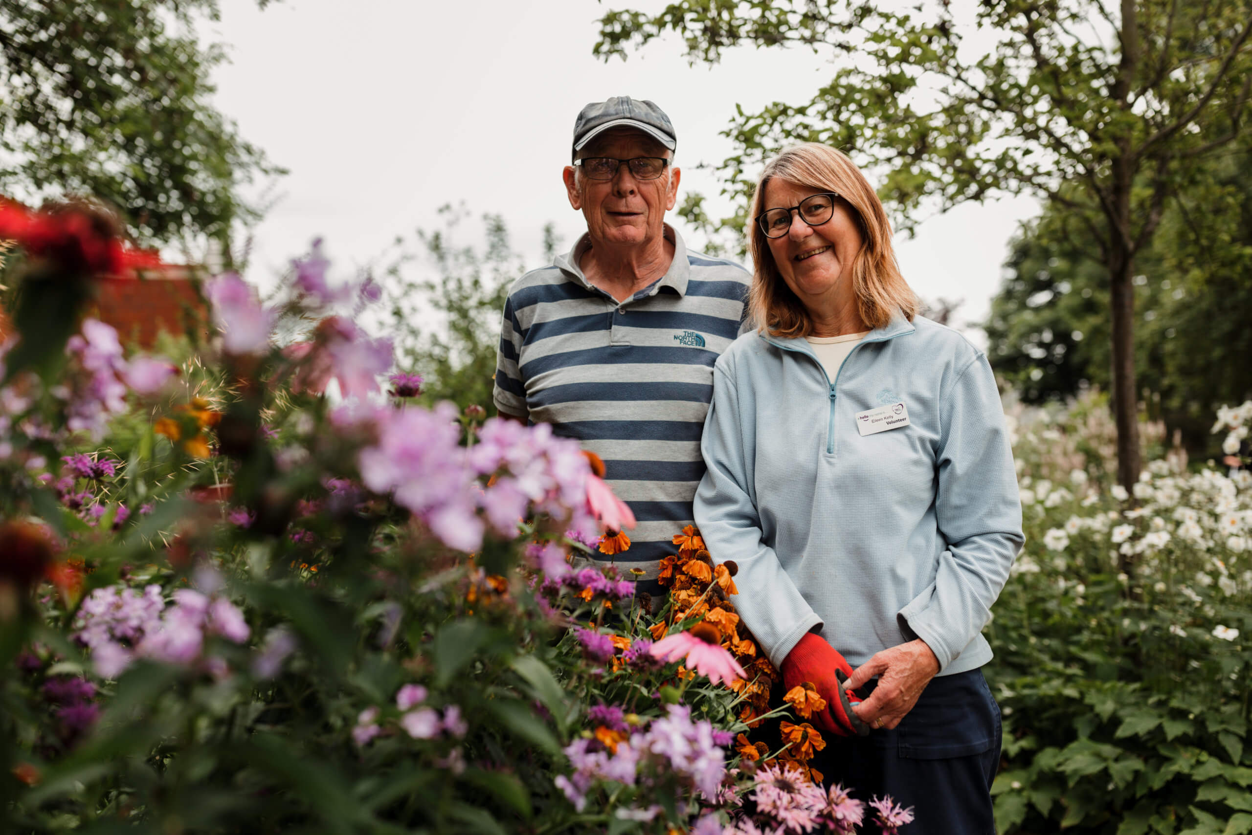 Male and female volunteer gardeners stood in front of flowers in the hospice grounds