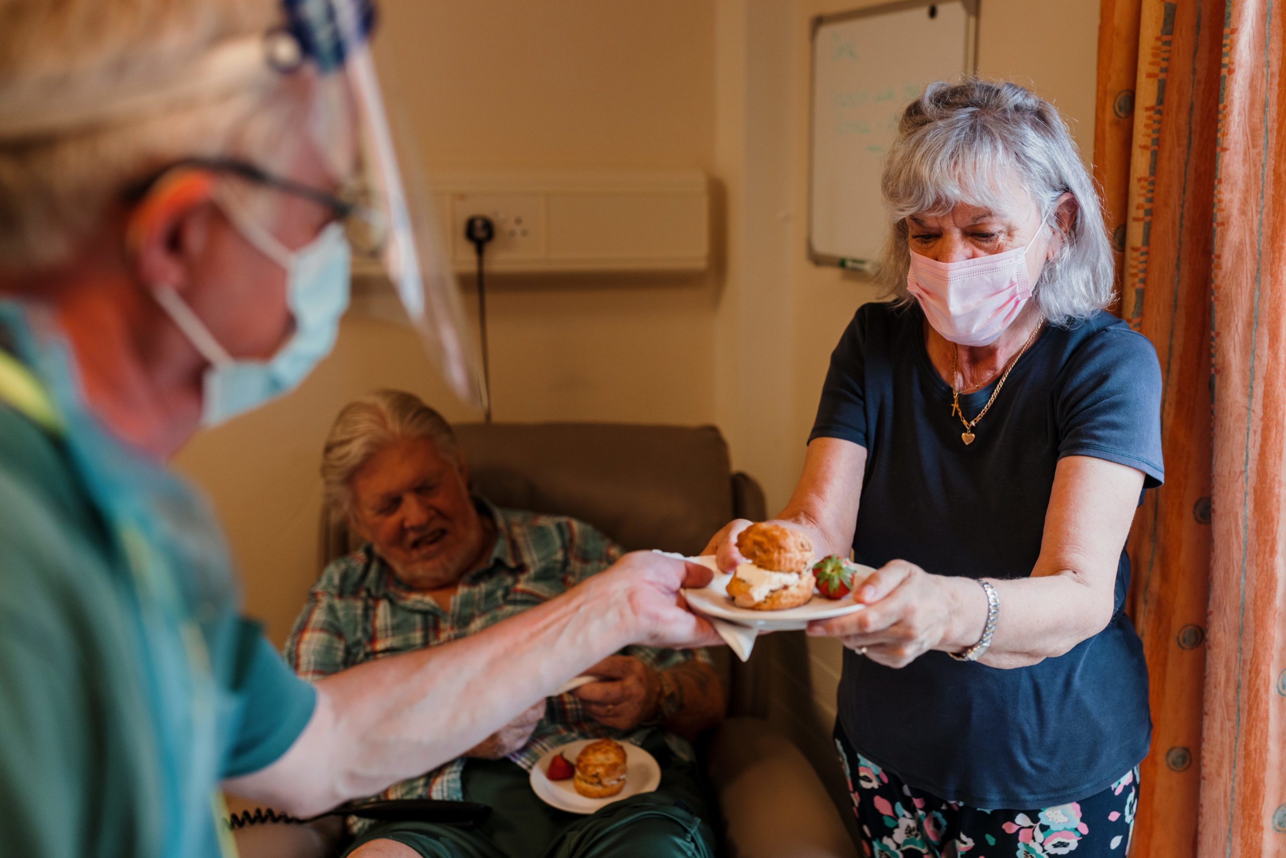 A volunteer in PPE handing a scone to a lady and man