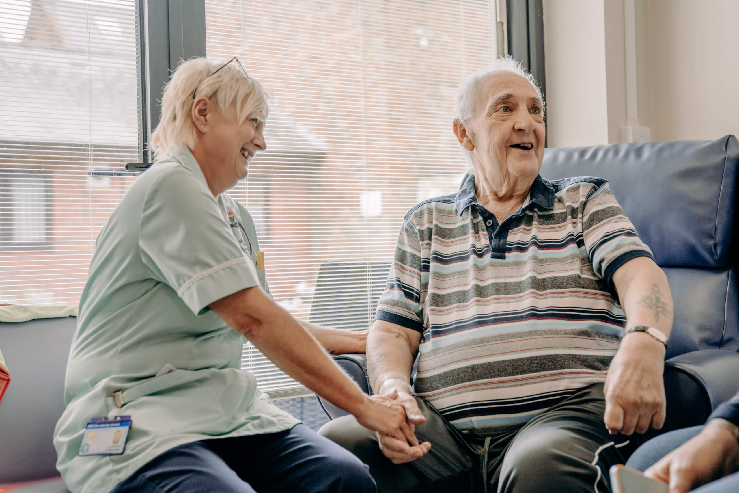 Healthcare Assistant holding the hand of a male patient and laughing together