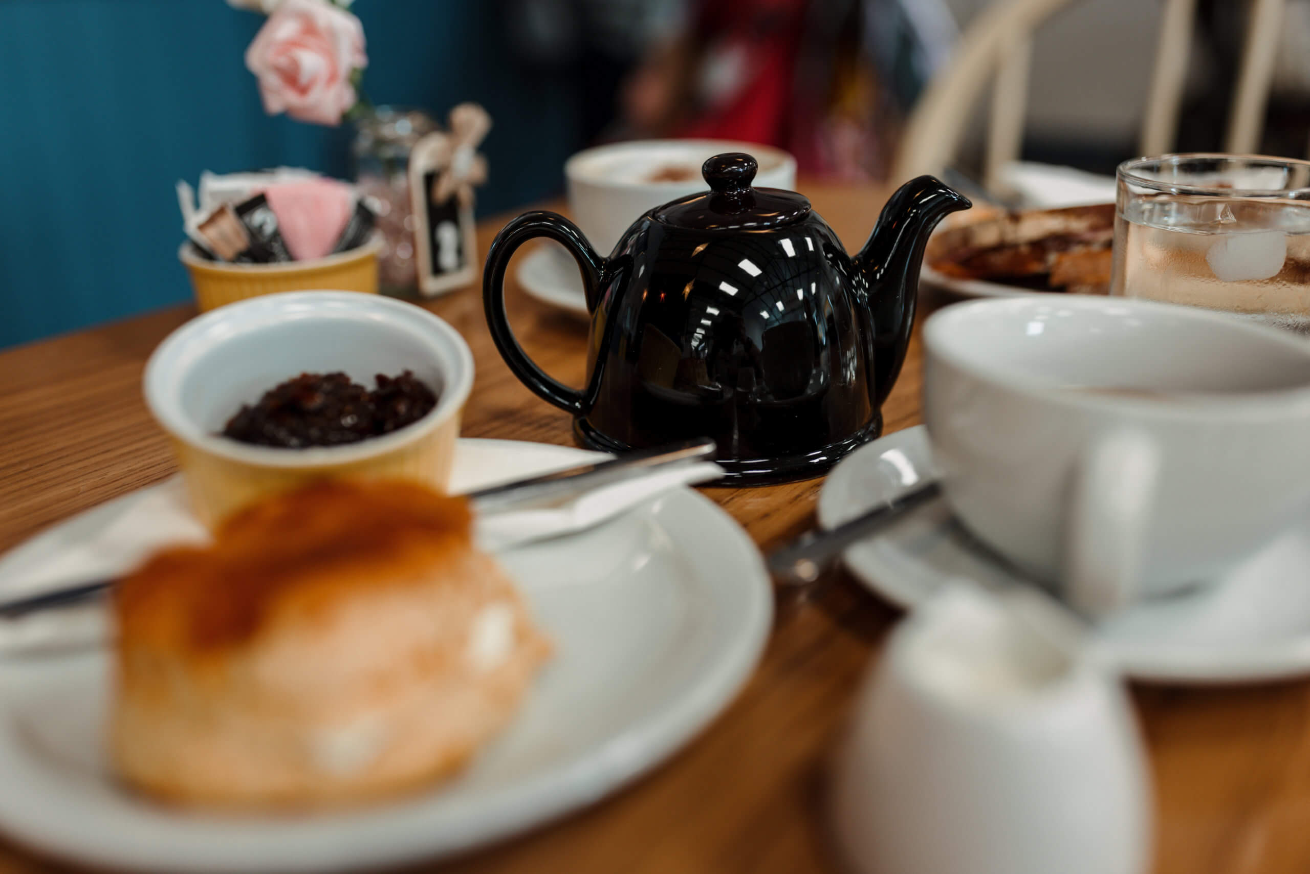 A scone, teapot and teacups on a table in a cafe