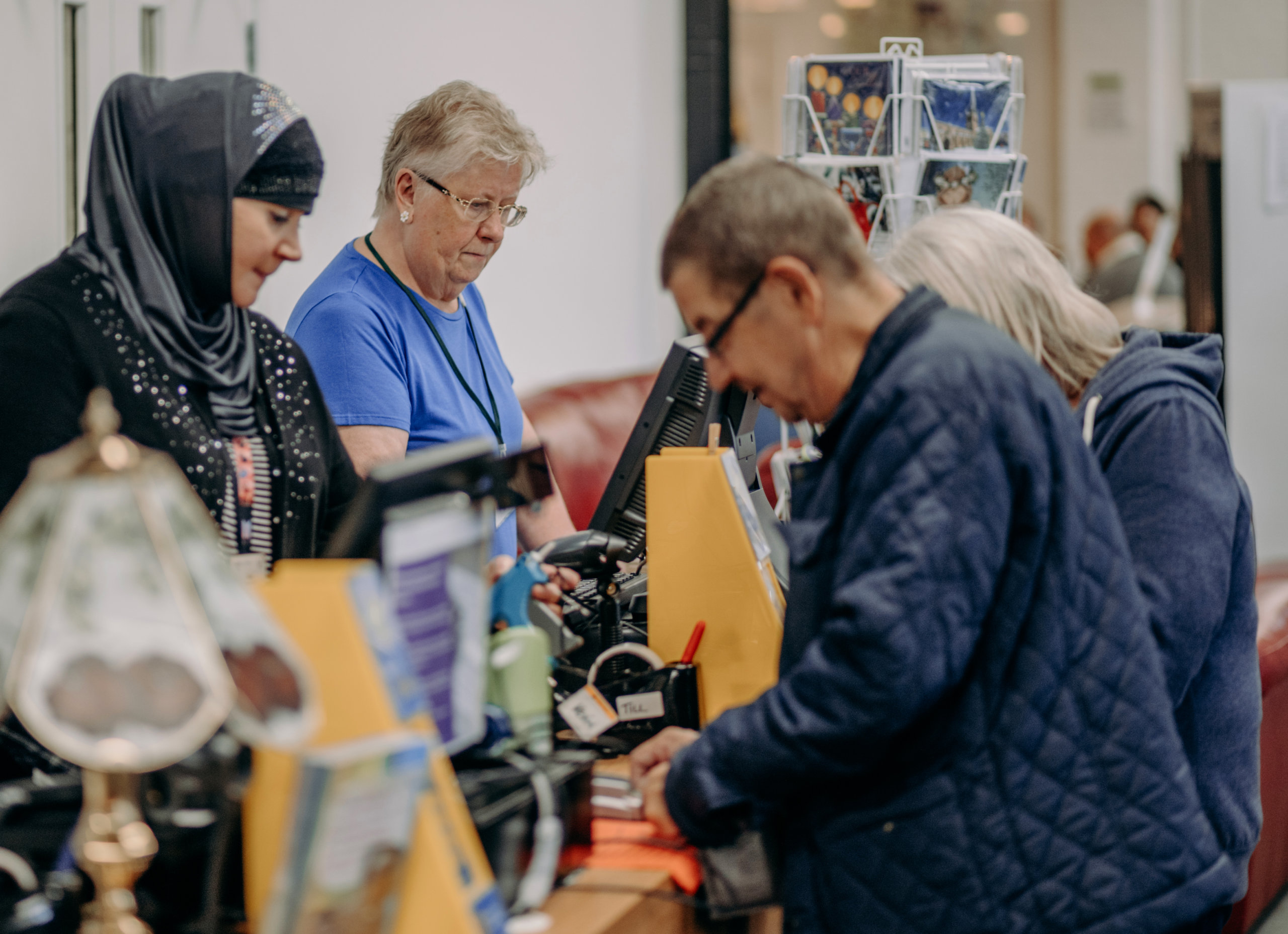 Two customers and two staff members serving at a till point