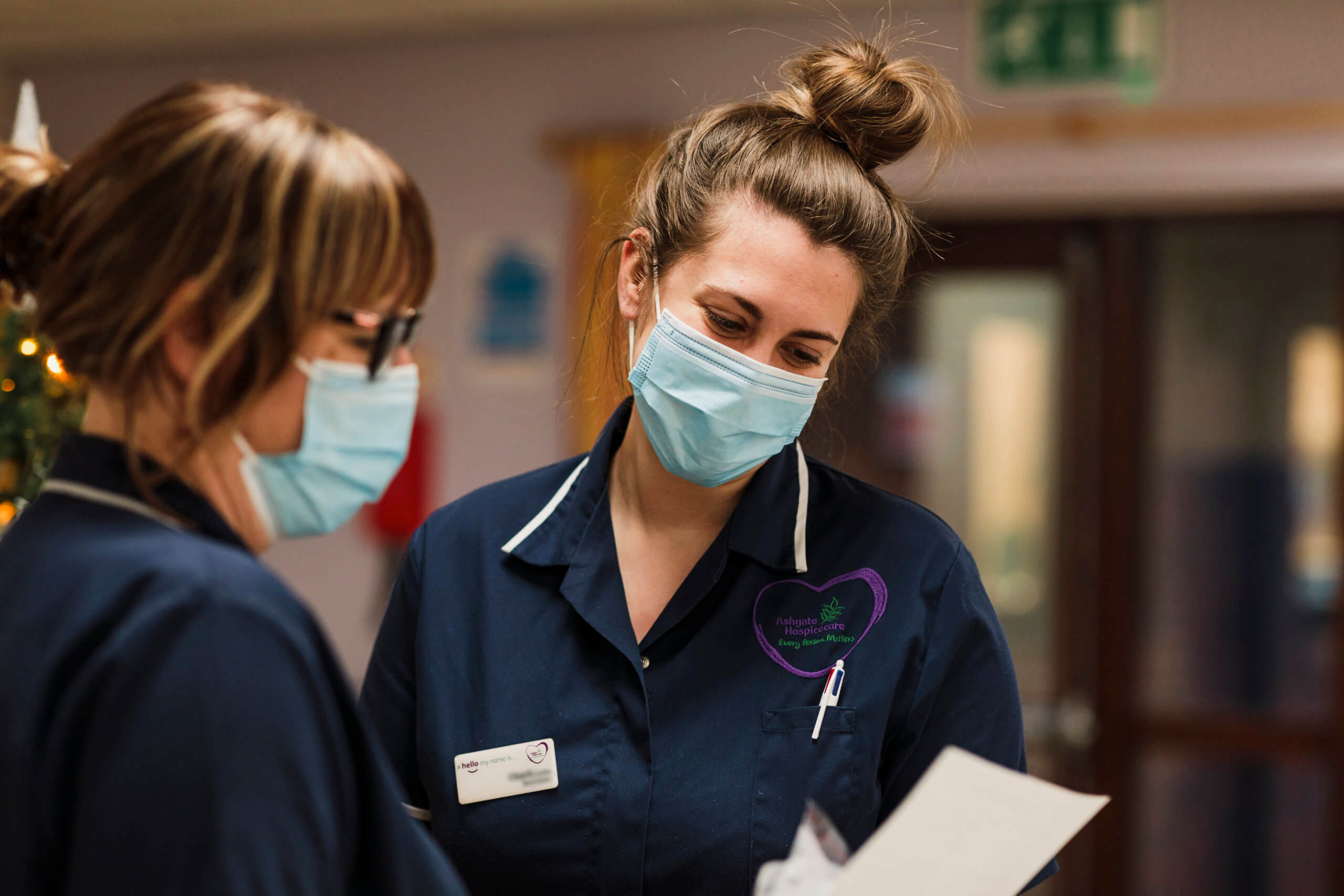 Two nurses wearing face masks looking down at a sheet of paper
