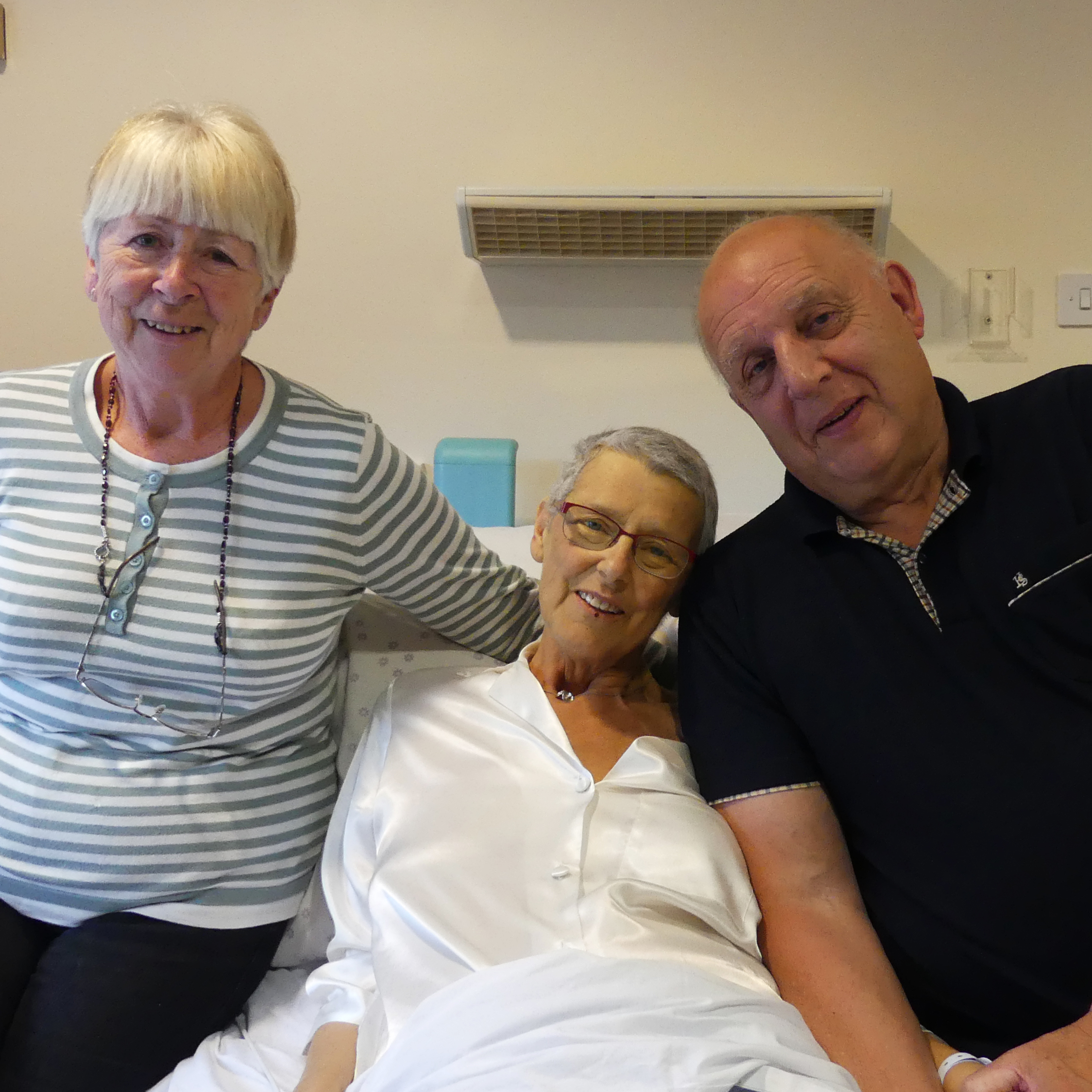 Ashgate Hospice patient in bed with two loved ones either side of her smiling