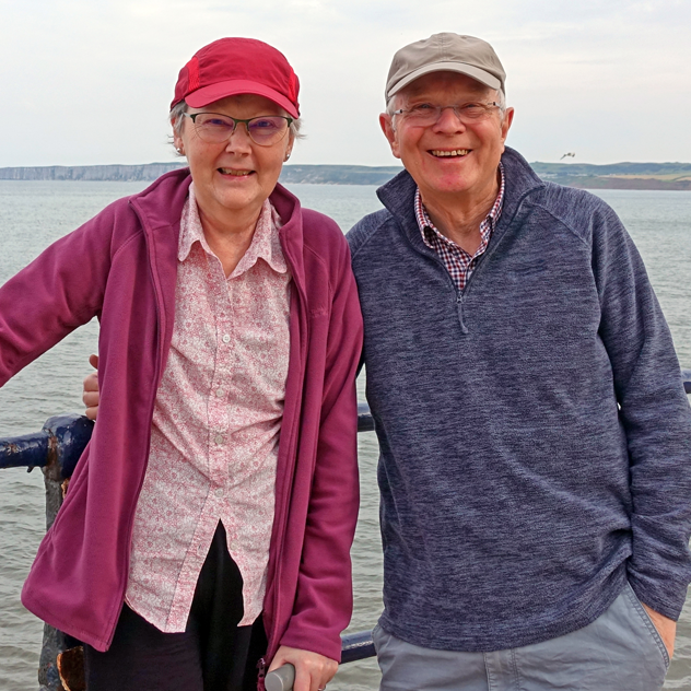Man and woman stand together with a lake in the background.