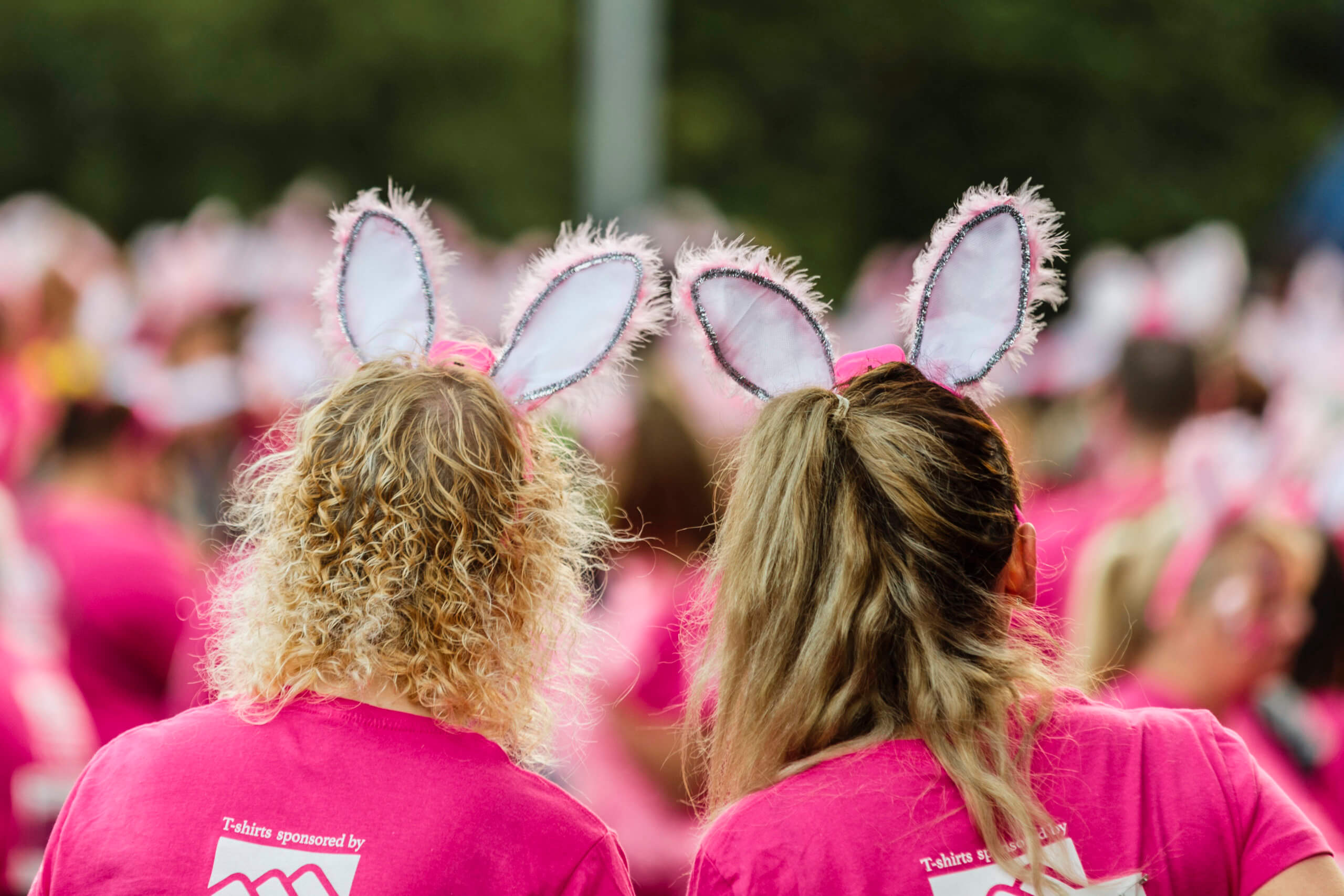 Two ladies in pink t-shirts and bunny ears with their back to the camera