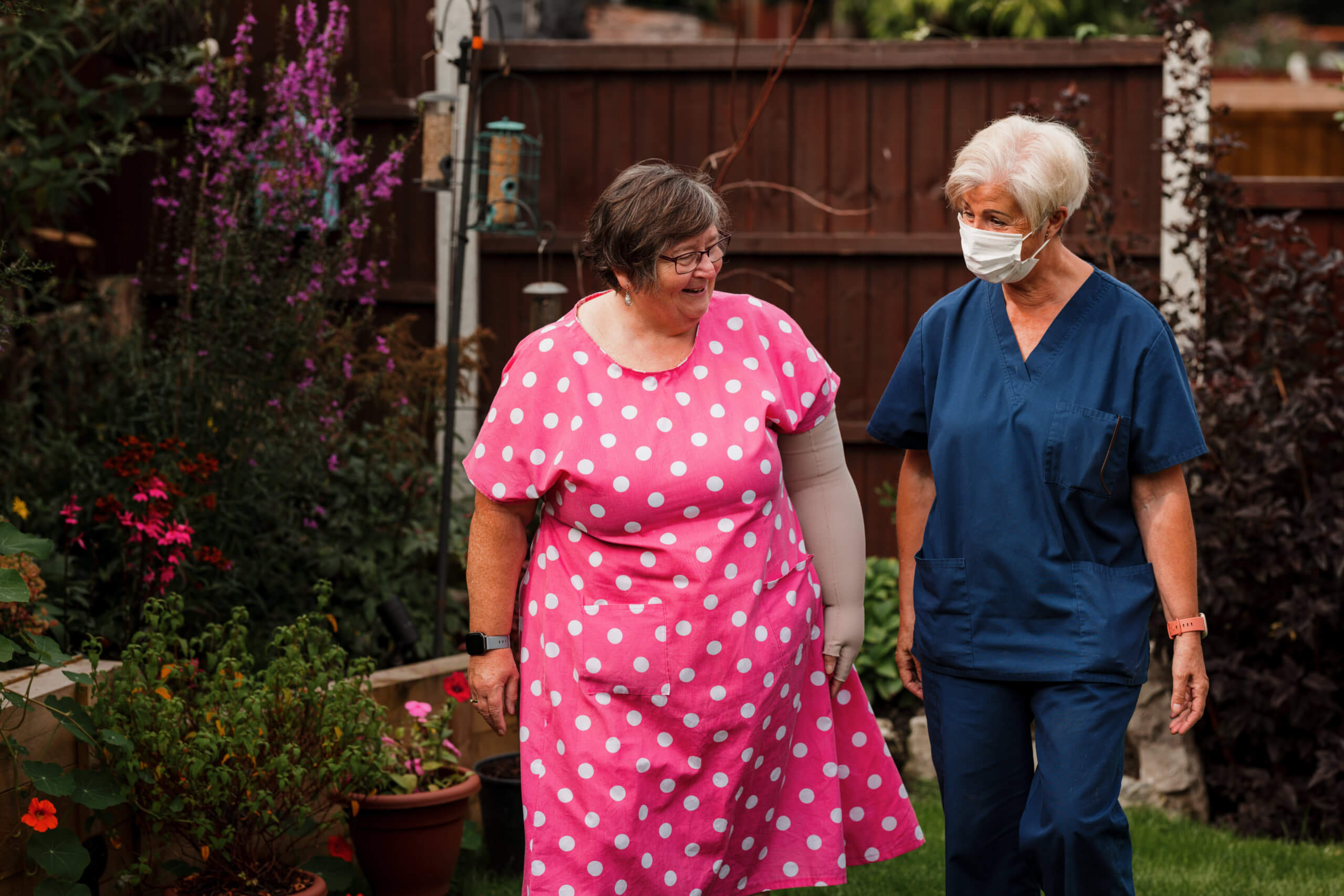 Lady in a pink dress walking in her garden with an Ashgate support worker