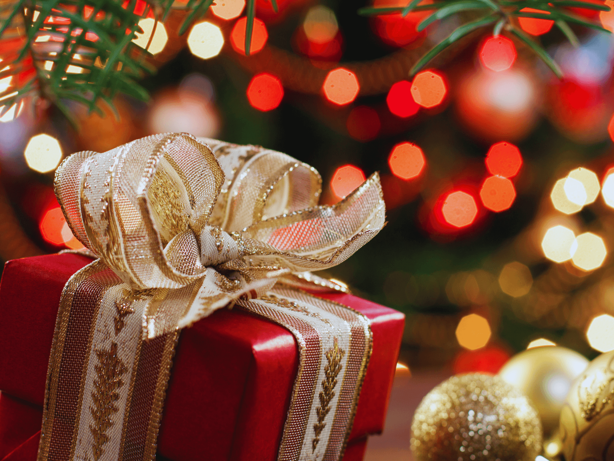 Christmas gift wrapped in red paper and a gold ribbon under a tree