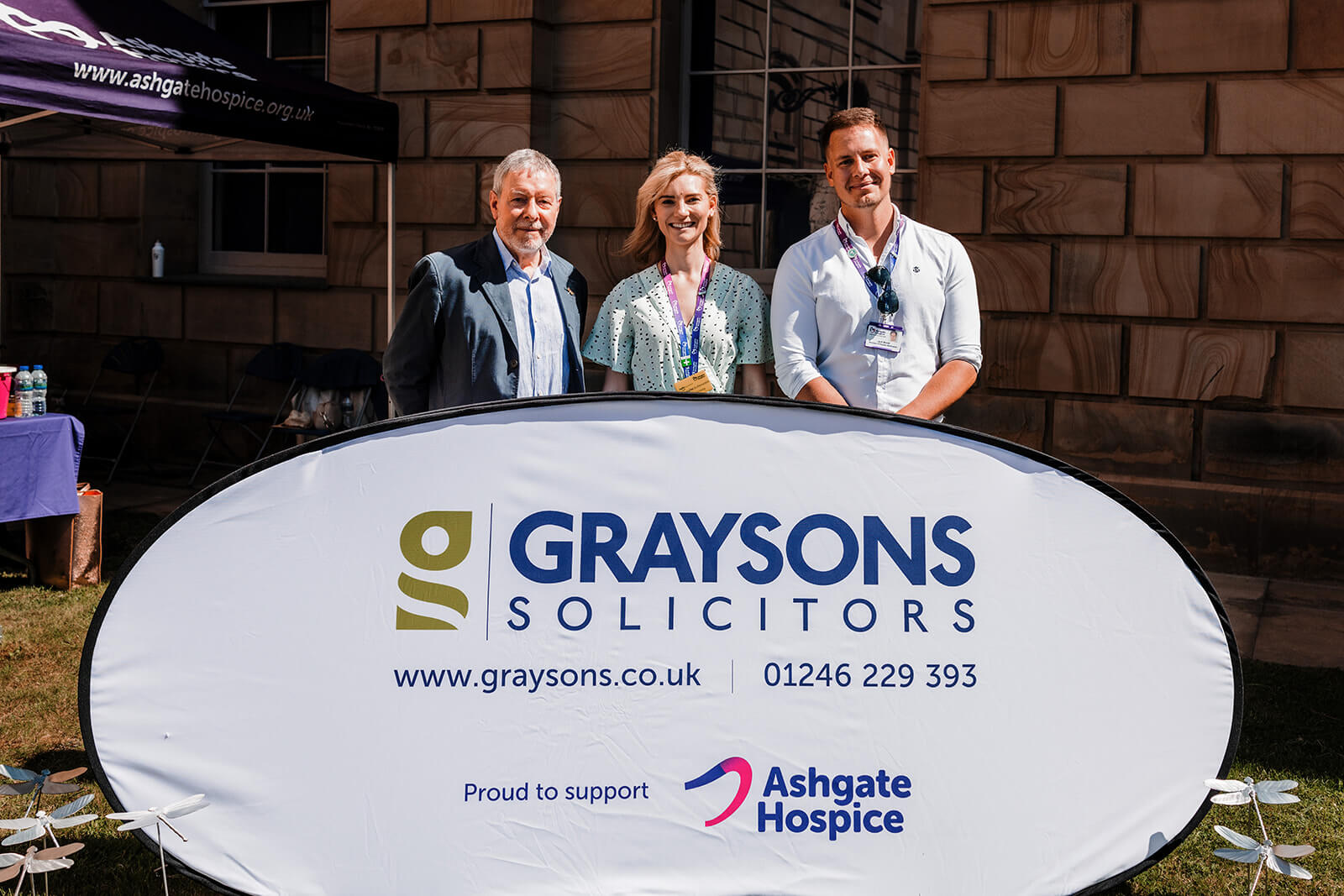 Three people stand behind a Graysons Solicitors banner