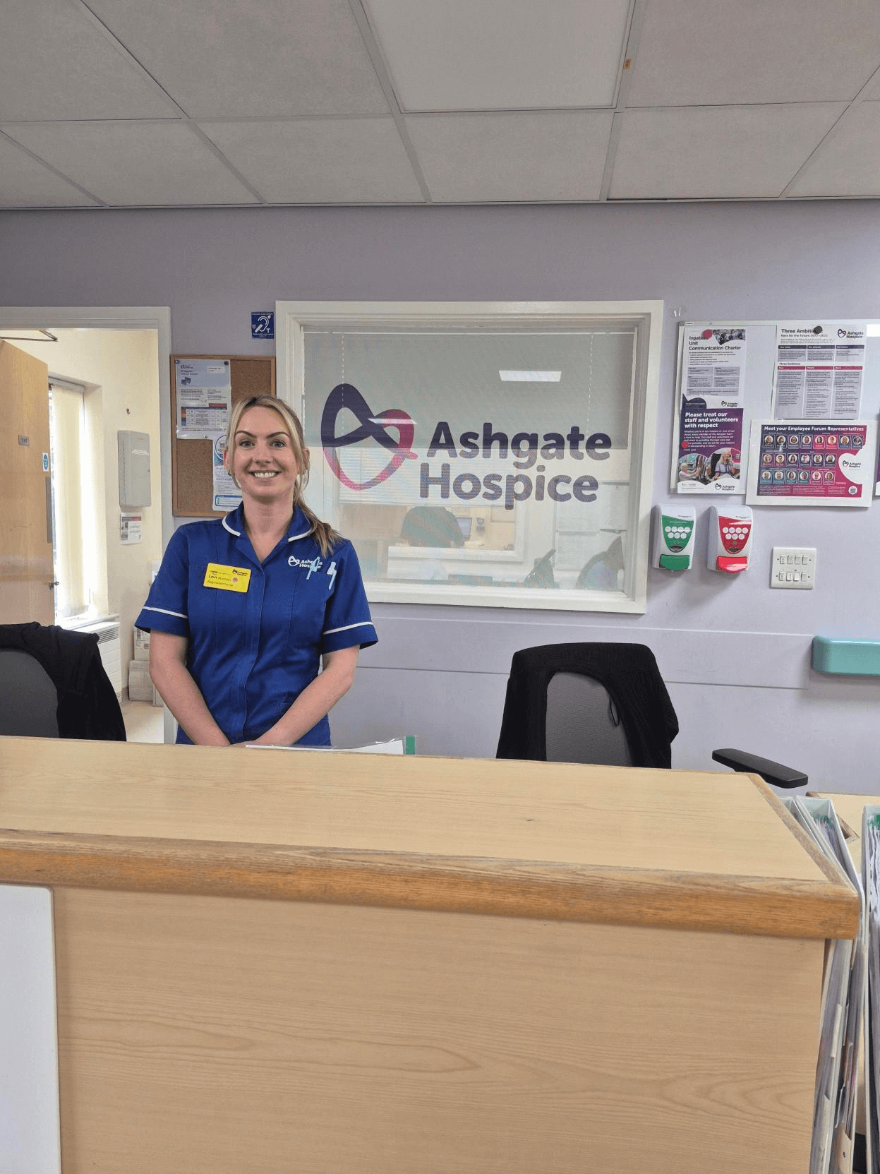 An Ashgate Hospice Nurse in uniform stood at the front desk on the Inpatient Unit,