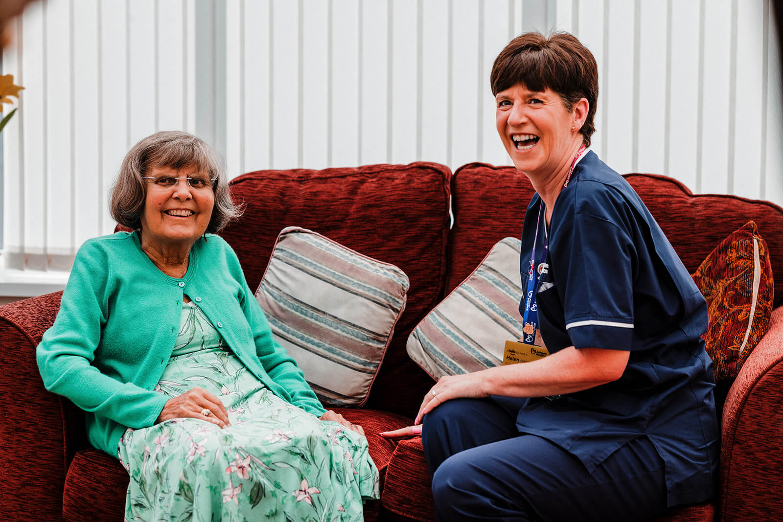Ashgate hospice nurse sits with a patient in their own home. They are sat on a sofa.